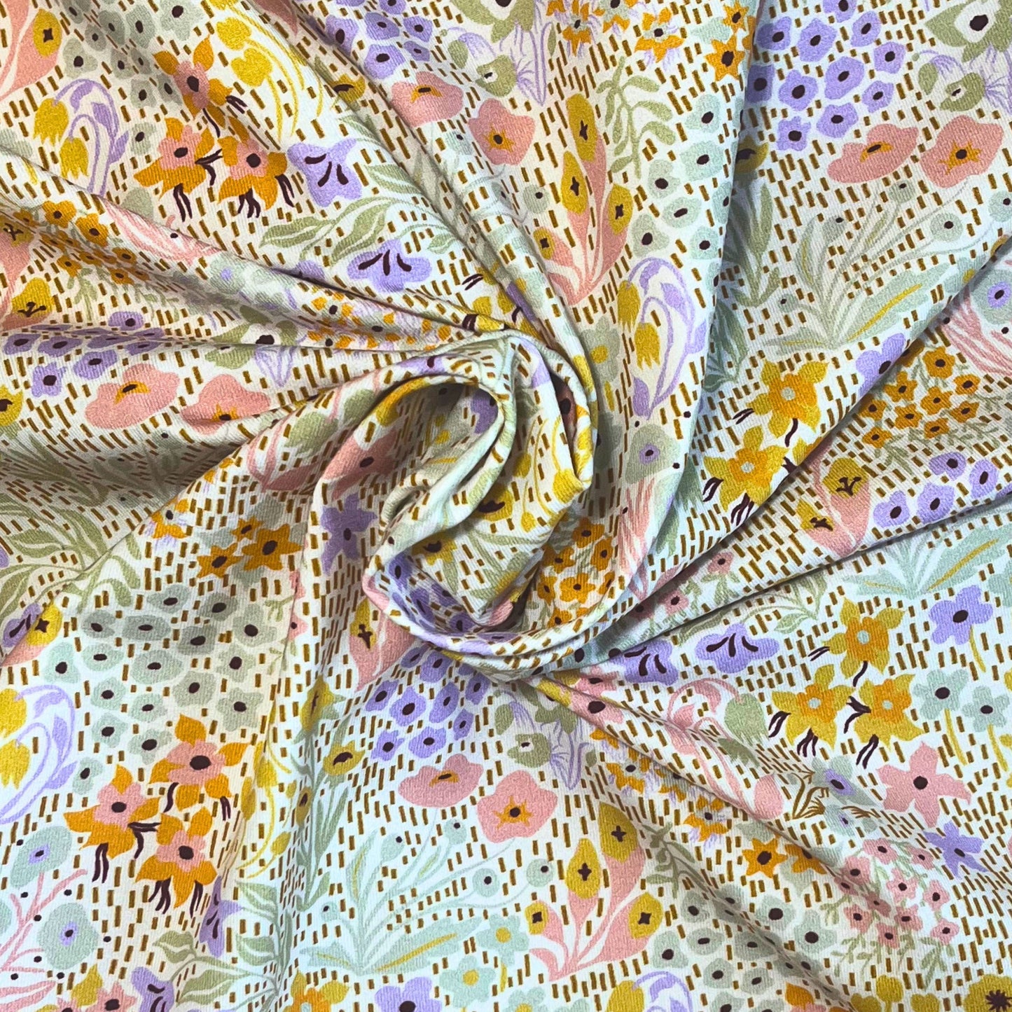 Close-up of floral digital print jersey fabric showing light pinks, lilacs, yellows, and greens – ideal for spring sewing projects.