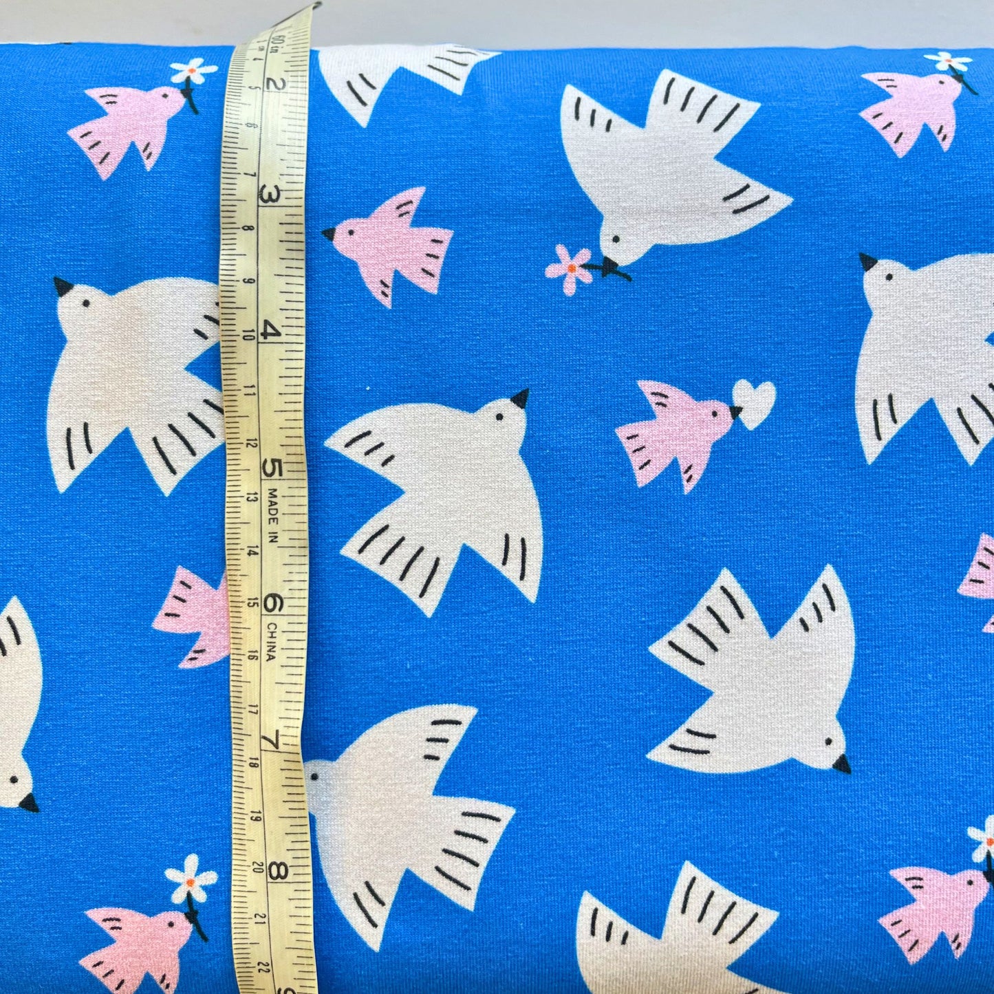 Daisy Bird print cotton jersey in vivid blue with white and pink birds folded to show soft knit construction — digitally printed 100% cotton fabric ideal for handmade leggings, dresses, tops and children's garments