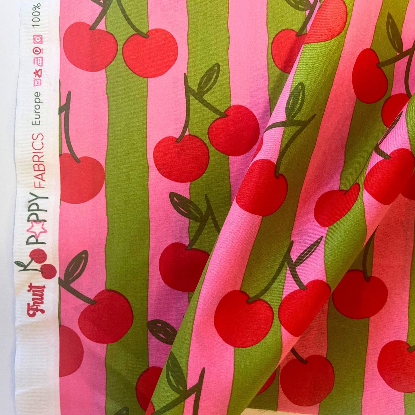 Lightweight cotton poplin with cheerful cherry design and pastel pink and green stripe background, perfect for handmade summer clothing.