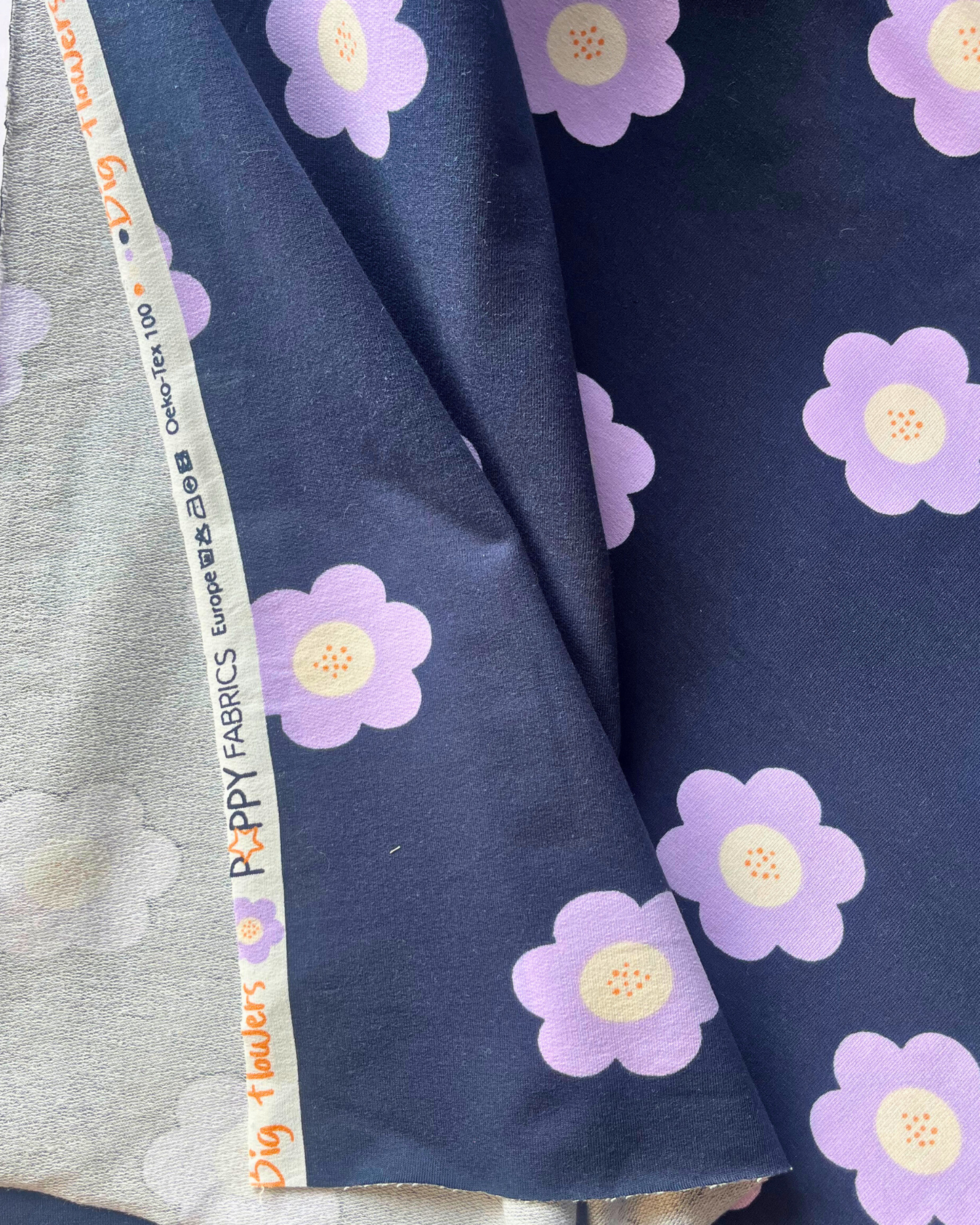 Bold lilac flower print on deep navy French terry fabric, shown folded to reveal soft looped reverse — a striking slow-fashion fabric for sweatshirts, co-ord sets and more