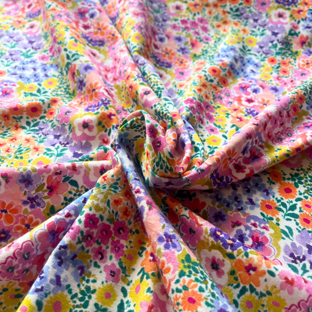 Close-up of multicolour ditsy floral digital print on stretch jersey fabric, showing densely packed garden bloom design and smooth knit construction — Oeko-Tex 100 certified cotton elastane