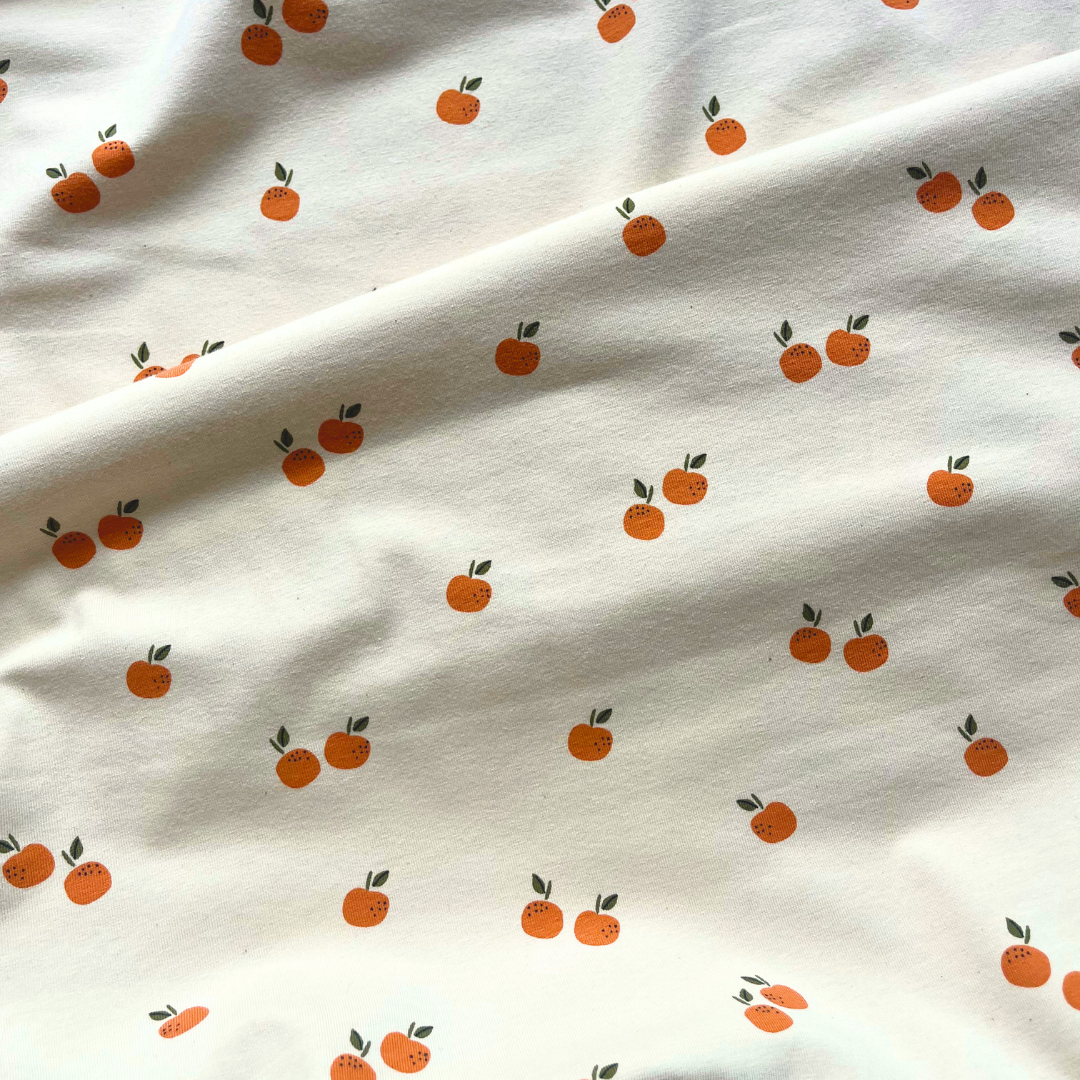 Flat lay of fruits print stretch jersey in warm cream, draped to show 200gsm weight and stretch — certified organic cotton fabric perfect for handmade tees, rompers and baby gifts