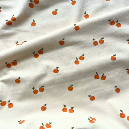 Flat lay of fruits print stretch jersey in warm cream, draped to show 200gsm weight and stretch — certified organic cotton fabric perfect for handmade tees, rompers and baby gifts