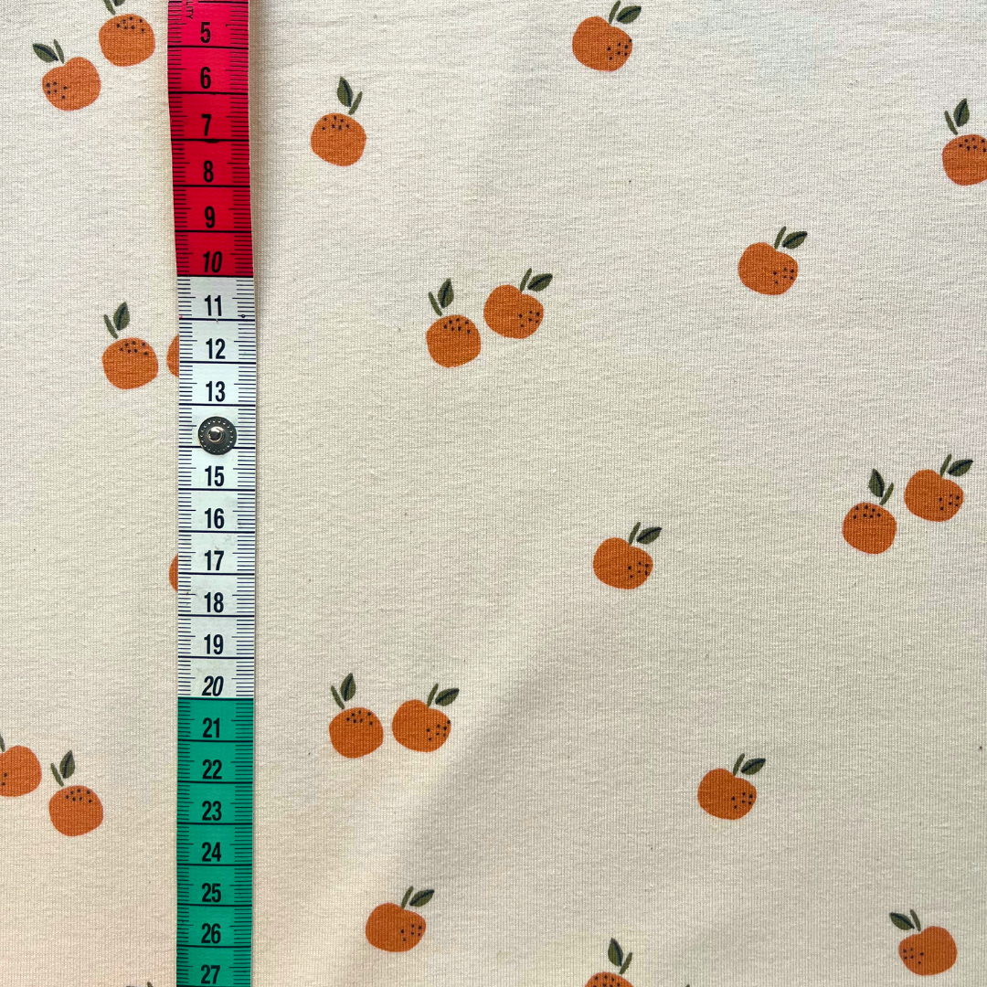 Close-up of cream single jersey fabric showing small scattered fruit and orange print — GOTS organic and Oeko-Tex 100 certified cotton elastane stretch fabric for babywear and children's sewing