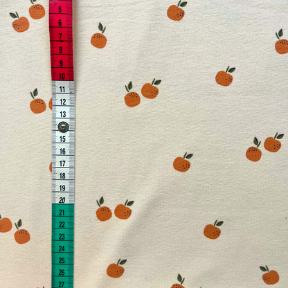 Close-up of cream single jersey fabric showing small scattered fruit and orange print — GOTS organic and Oeko-Tex 100 certified cotton elastane stretch fabric for babywear and children's sewing