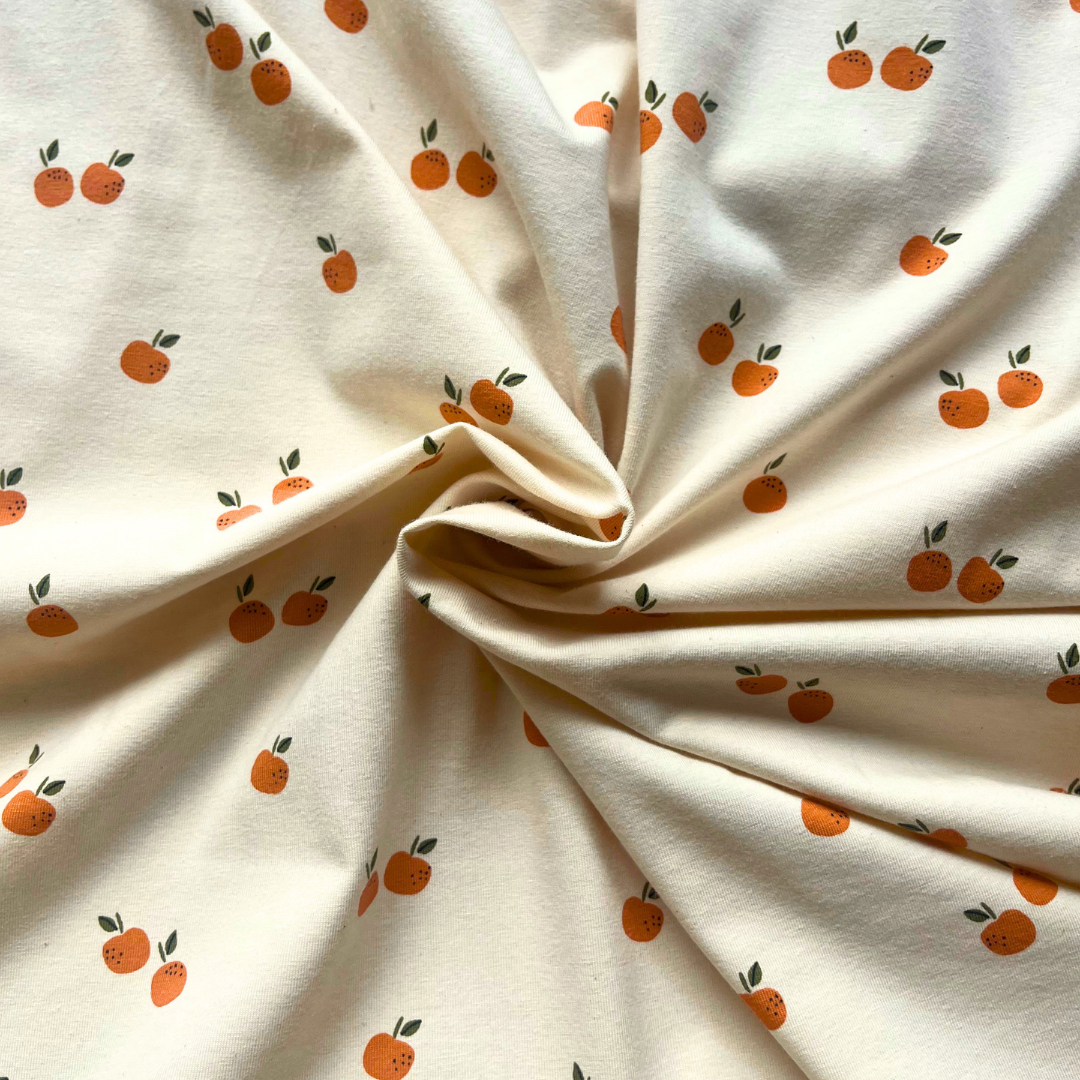 Cream organic cotton stretch jersey with cheerful small fruit print folded to show fabric weight — ideal for handmade baby bodysuits, children's clothing and relaxed adult tops