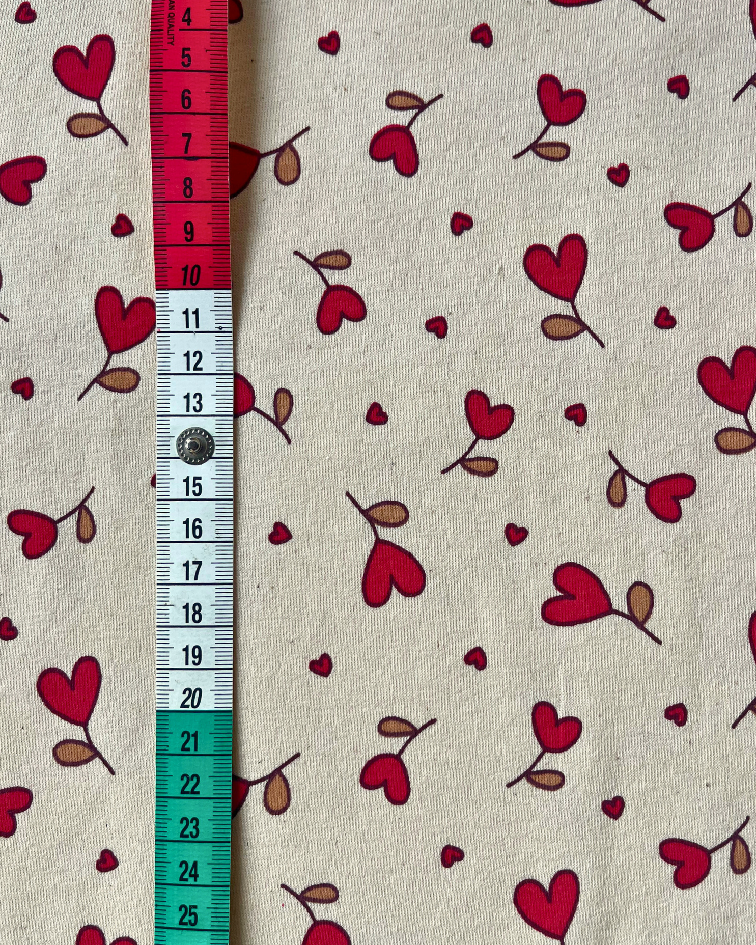 Flat lay of Natural Hearts sweatshirting fabric showing warm cream base with delicate red heart print, 95% cotton elastane blend for babywear and children's sewing