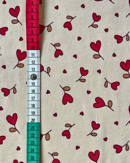 Flat lay of Natural Hearts sweatshirting fabric showing warm cream base with delicate red heart print, 95% cotton elastane blend for babywear and children's sewing