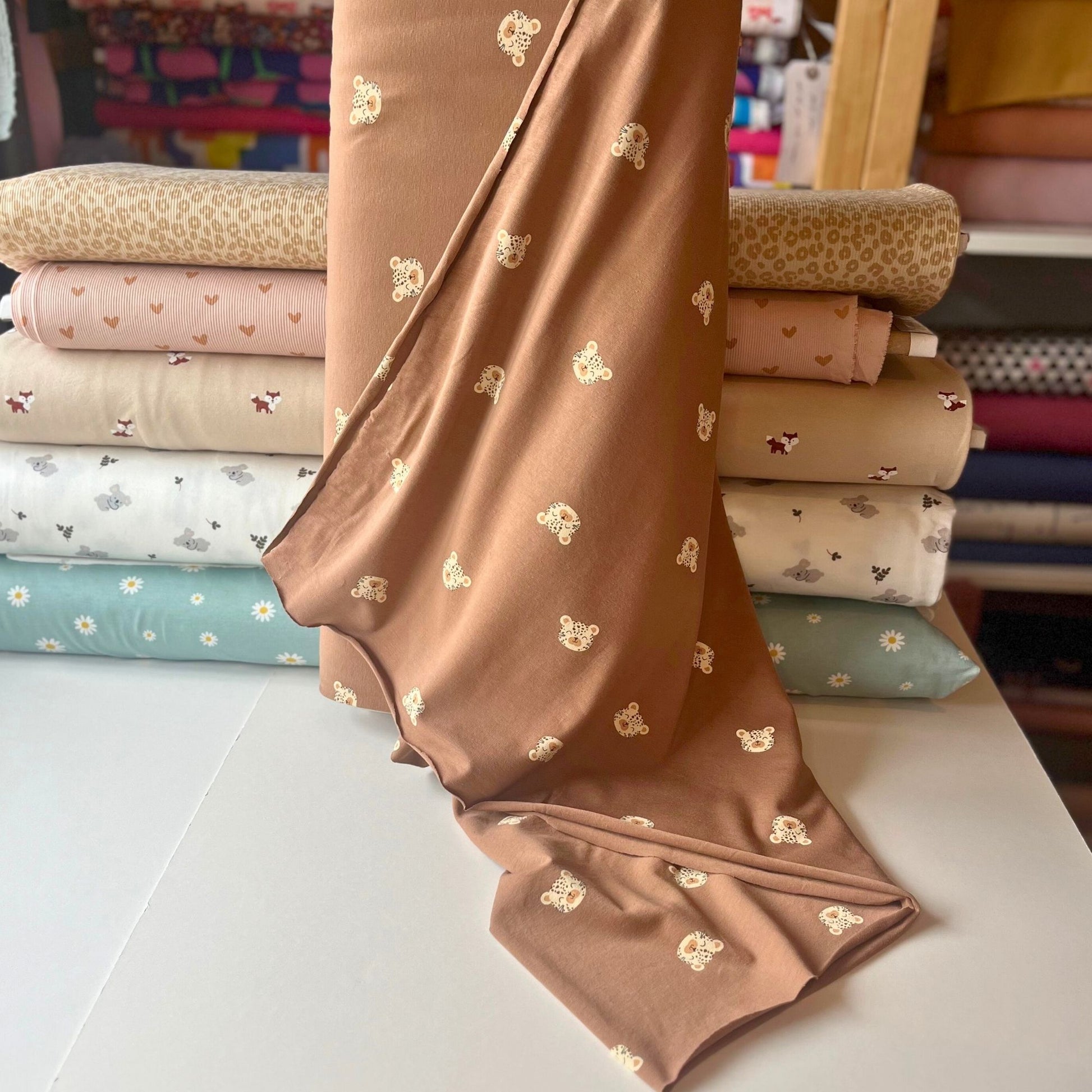 Leopard print cotton jersey fabric with cute illustrated leopard heads on brown background