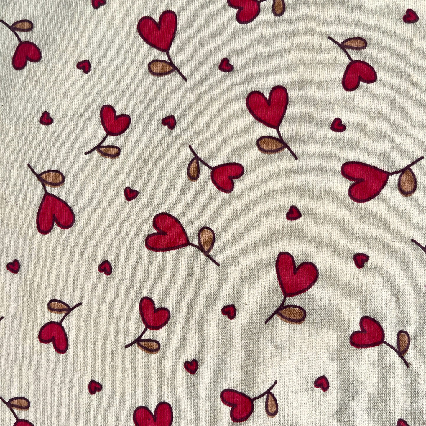 Close-up of supersoft brushed sweatshirting in natural and red, showing small scattered heart print on smooth fabric face and fluffy brushed reverse