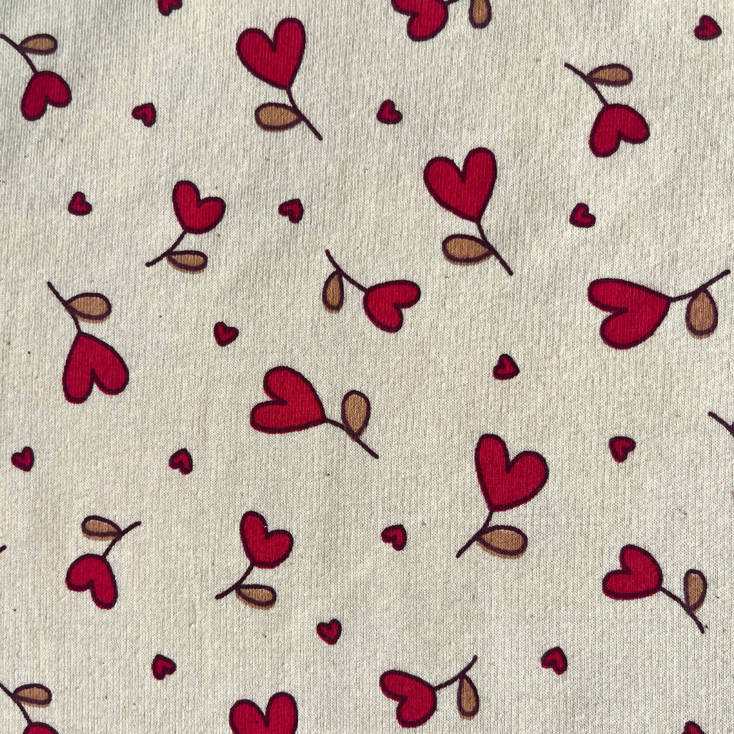Close-up of supersoft brushed sweatshirting in natural and red, showing small scattered heart print on smooth fabric face and fluffy brushed reverse