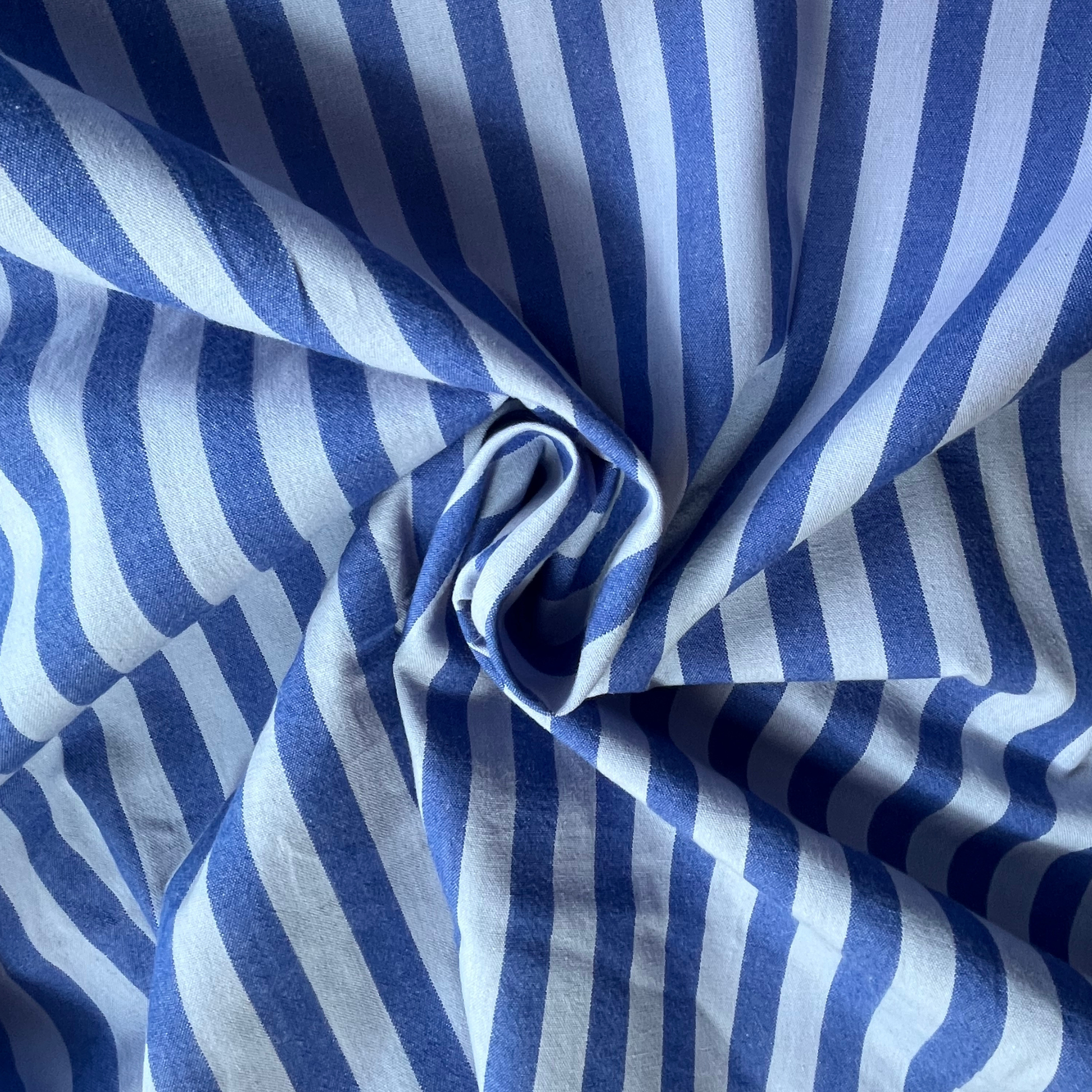 Blue denim shades in striped fabric draped in a central swirl, showing dressmaking cloth