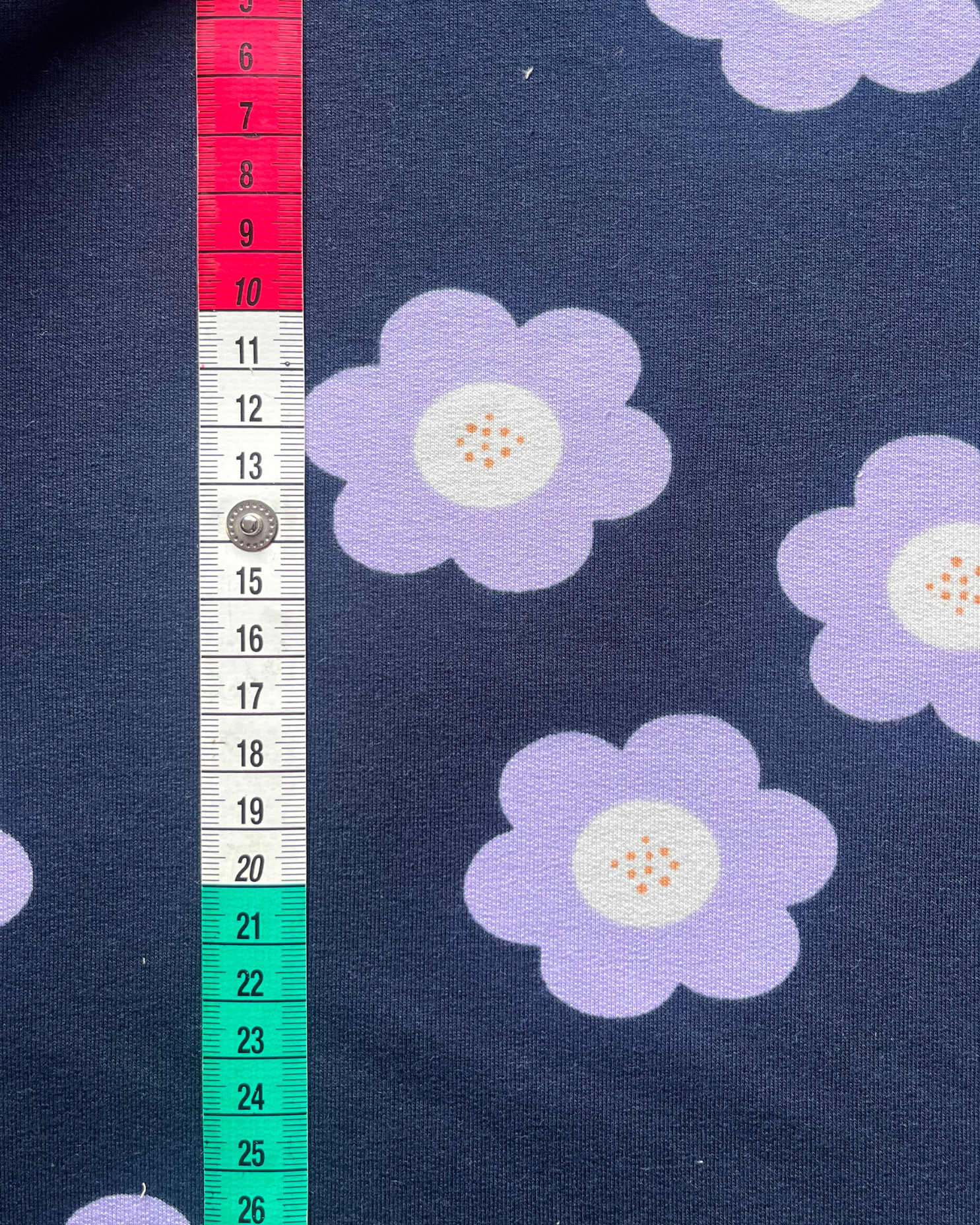 Close-up of navy French terry fabric showing large lilac flower print on smooth face, soft looped reverse visible at fold — 95% cotton 5% elastane sweatshirting