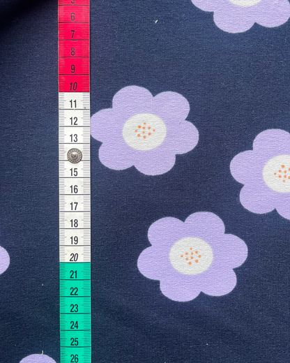 Close-up of navy French terry fabric showing large lilac flower print on smooth face, soft looped reverse visible at fold — 95% cotton 5% elastane sweatshirting