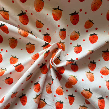	Cream and red strawberry print jersey fabric folded to show soft knit construction — digitally printed cotton elastane stretch fabric ideal for children's dresses, rompers and relaxed adult tops