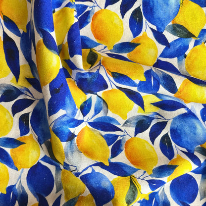 Close-up of white linen viscose fabric showing large bold lemon print in vivid yellow and fresh green — naturally textured breathable woven fabric ideal for slow fashion summer dressmaking
