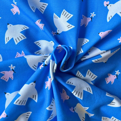 Close-up of bright blue digital cotton jersey fabric showing white and pink bird and floral print — crisp digitally printed 100% cotton knit ideal for slow fashion dressmaking and children's sewing