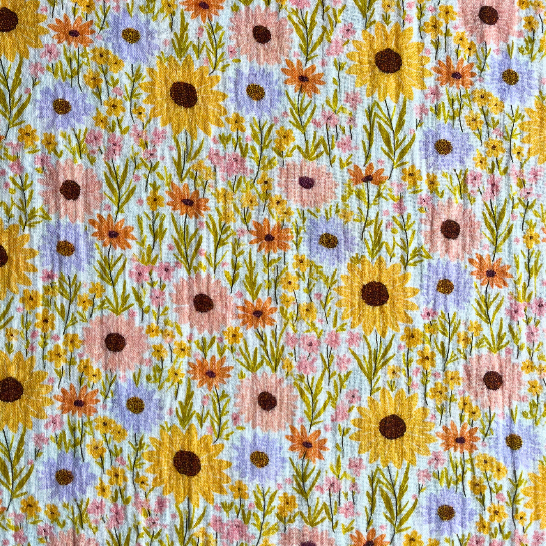 Flat lay of sunshine yellow double gauze fabric with painterly sunflower meadow print draped to show lightweight 125gsm drape — perfect for floaty handmade summer dresses and playsuits
