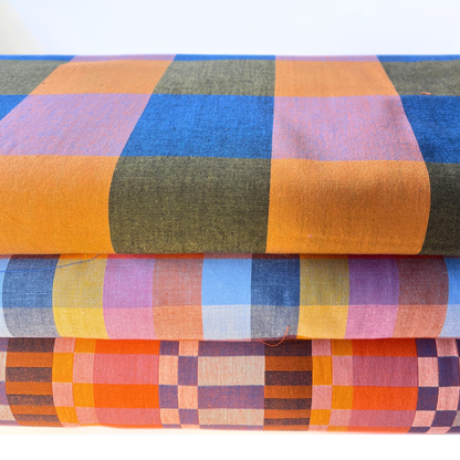 Three folded plaid fabrics stacked on top of each other, showcasing different multicolor patterns including orange, blue, green, pink, and yellow.