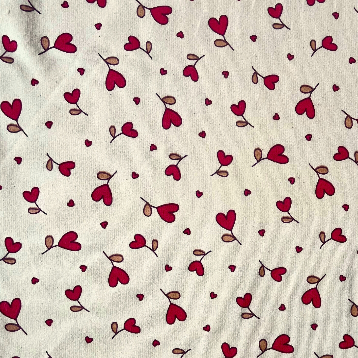 Close-up of supersoft brushed sweatshirting in natural and red, showing small scattered heart print on smooth fabric face and fluffy brushed reverse