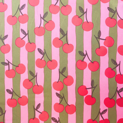 Close-up of Cherry Stripe Cotton Poplin fabric by Poppy Fabrics, featuring pink and green stripes with playful cherry print on 100% cotton.