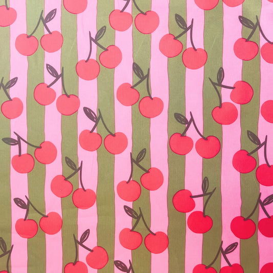 Close-up of Cherry Stripe Cotton Poplin fabric by Poppy Fabrics, featuring pink and green stripes with playful cherry print on 100% cotton.