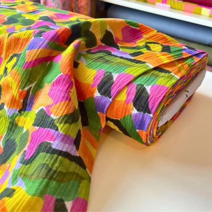 Flat lay of Tropical Palette double gauze fabric draped to show featherlight 125gsm weight and soft two-layer construction — expressive botanical paint streak print in tropical colours perfect for handmade summer dresses and playsuits