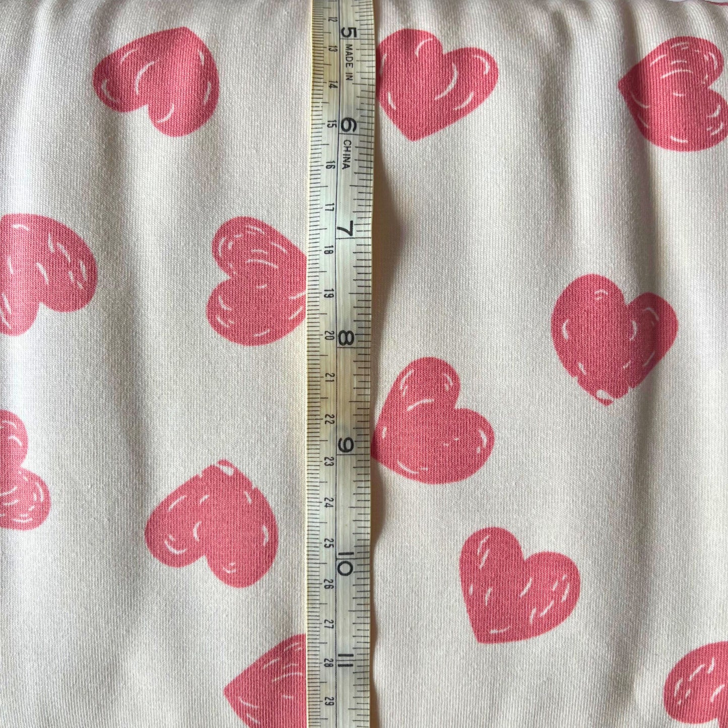 Flat lay of cream doodle hearts jersey fabric draped to show 200gsm weight and stretch — spontaneous hand-drawn rose pink heart print perfect for handmade children's slow fashion sewing and baby gifts