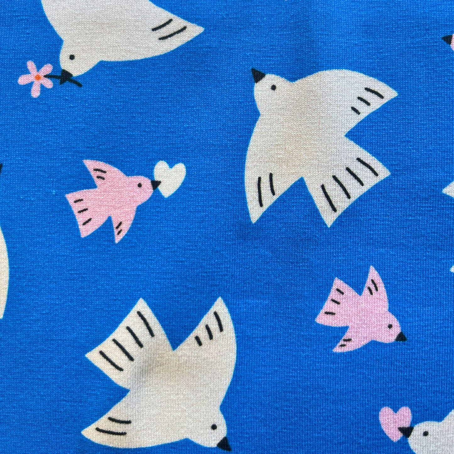 Flat lay of Daisy Bird cotton jersey in bold blue with white and pink birds in flight, draped to show soft knit weight and stretch — perfect for handmade t-shirts, jersey dresses and children's tops