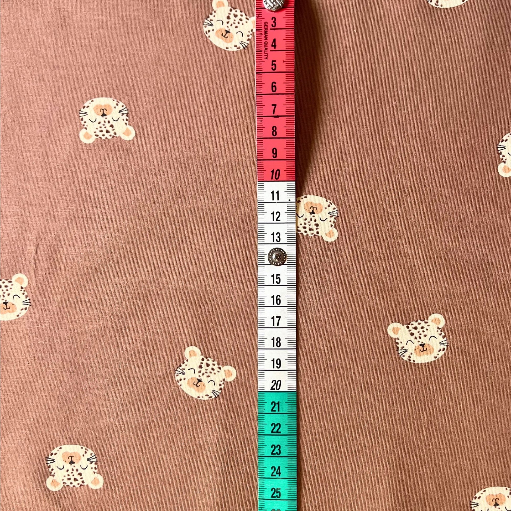 Close-up of playful leopard face print on warm earthy toned knit fabric.