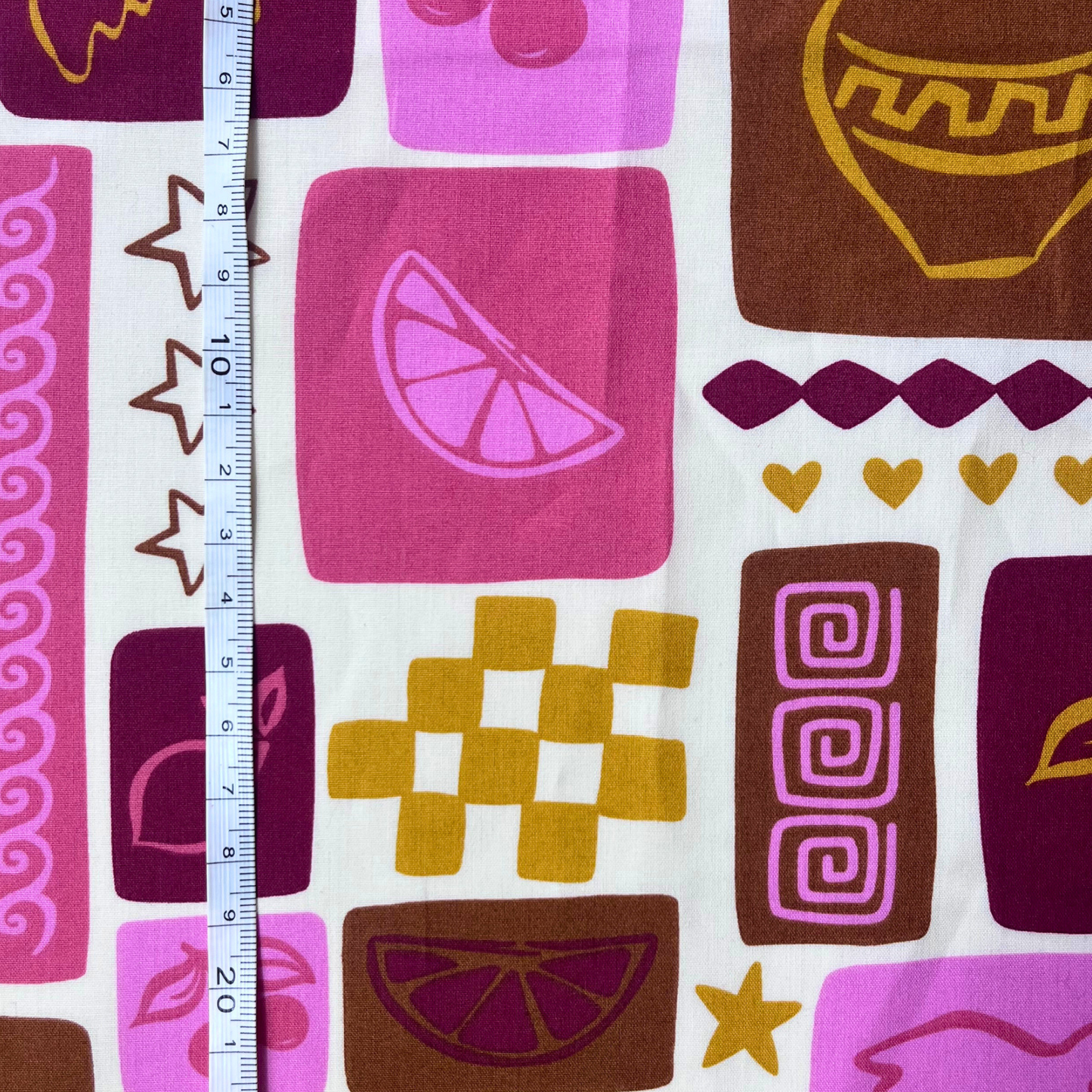 Flat lay of Poppy Fabrics summer patchwork poplin in off white draped to show crisp lightweight 110gsm drape — holiday inspired print with shells, suns, birds and fruit in warm summer tones, perfect for handmade shirt dresses and statement co-ords