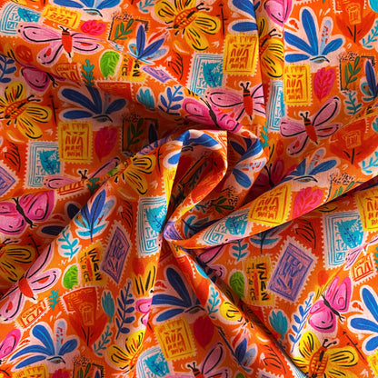 Flat lay of Empee Studio Postcard Garden cotton fabric in orange draped to show crisp woven texture — scattered botanical and butterfly print perfect for handmade summer dresses, blouses and children's pinafores