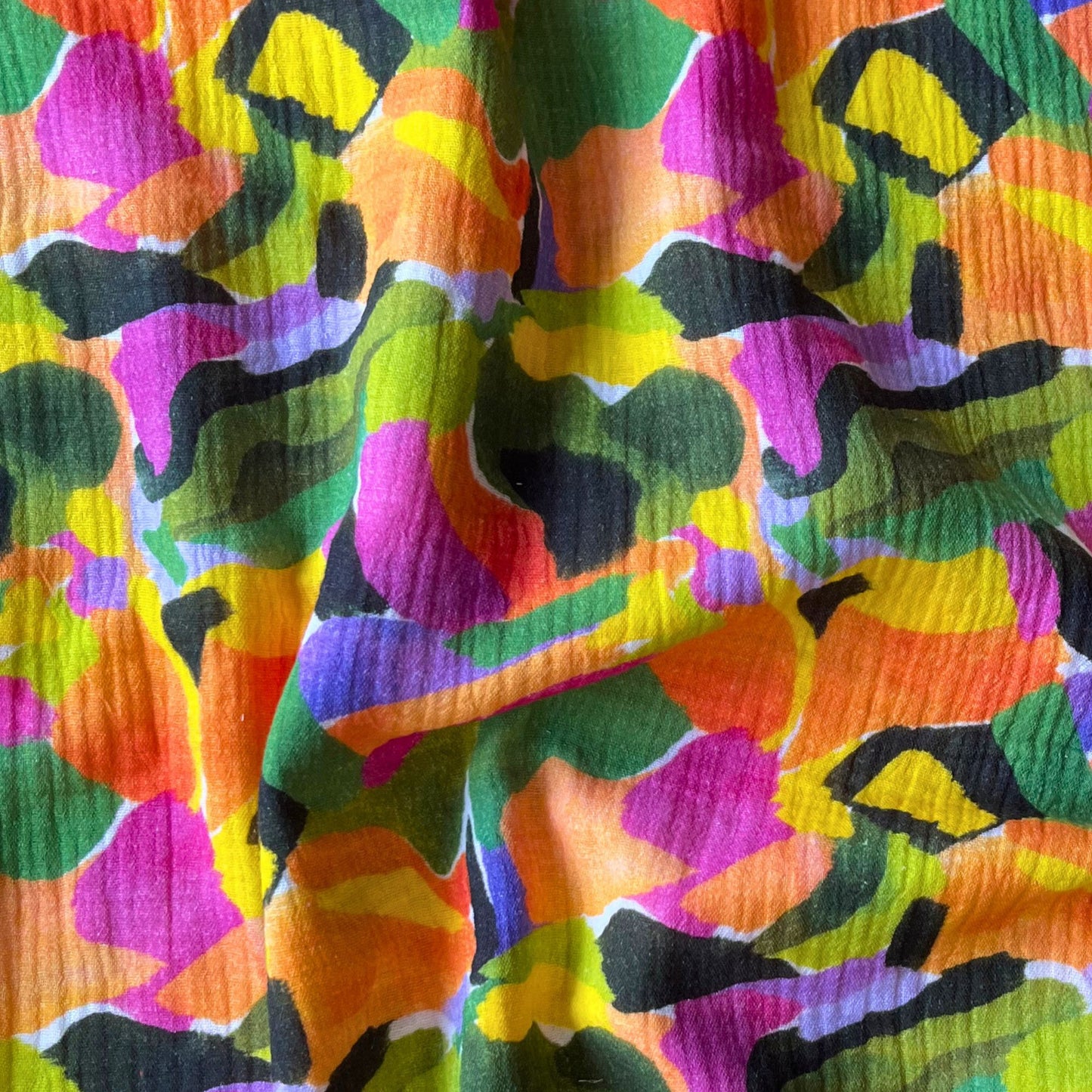White double gauze fabric with bold paint streak botanical print in tropical greens, purples and oranges — soft breathable 100% cotton two-layer woven for slow fashion dressmaking, children's clothing and baby gifts