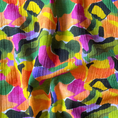 White double gauze fabric with bold paint streak botanical print in tropical greens, purples and oranges — soft breathable 100% cotton two-layer woven for slow fashion dressmaking, children's clothing and baby gifts