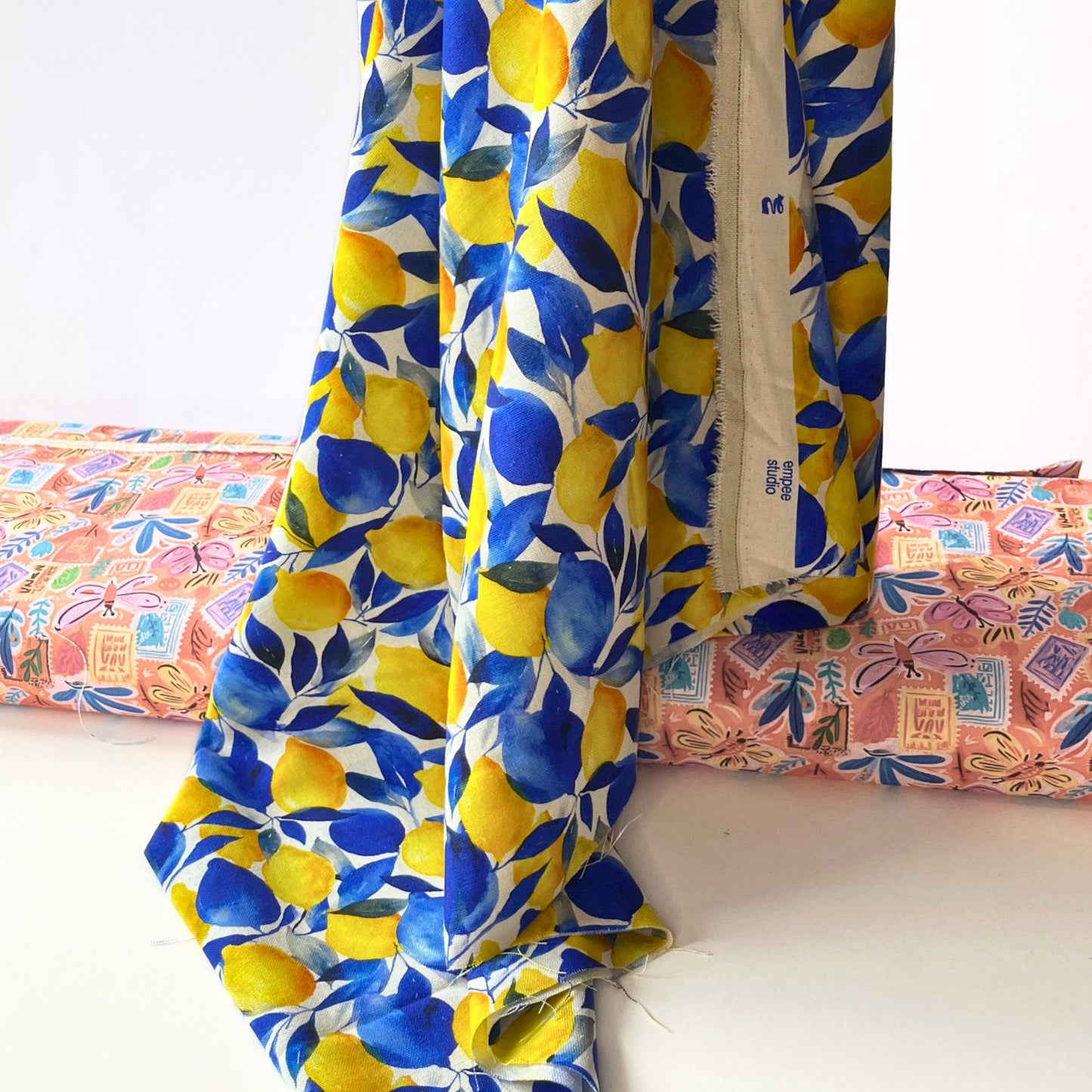 White linen viscose fabric with large bold yellow lemon and green foliage print folded to show natural woven texture — breathable Mediterranean print fabric ideal for handmade blouses, wide-leg trousers and summer dresses