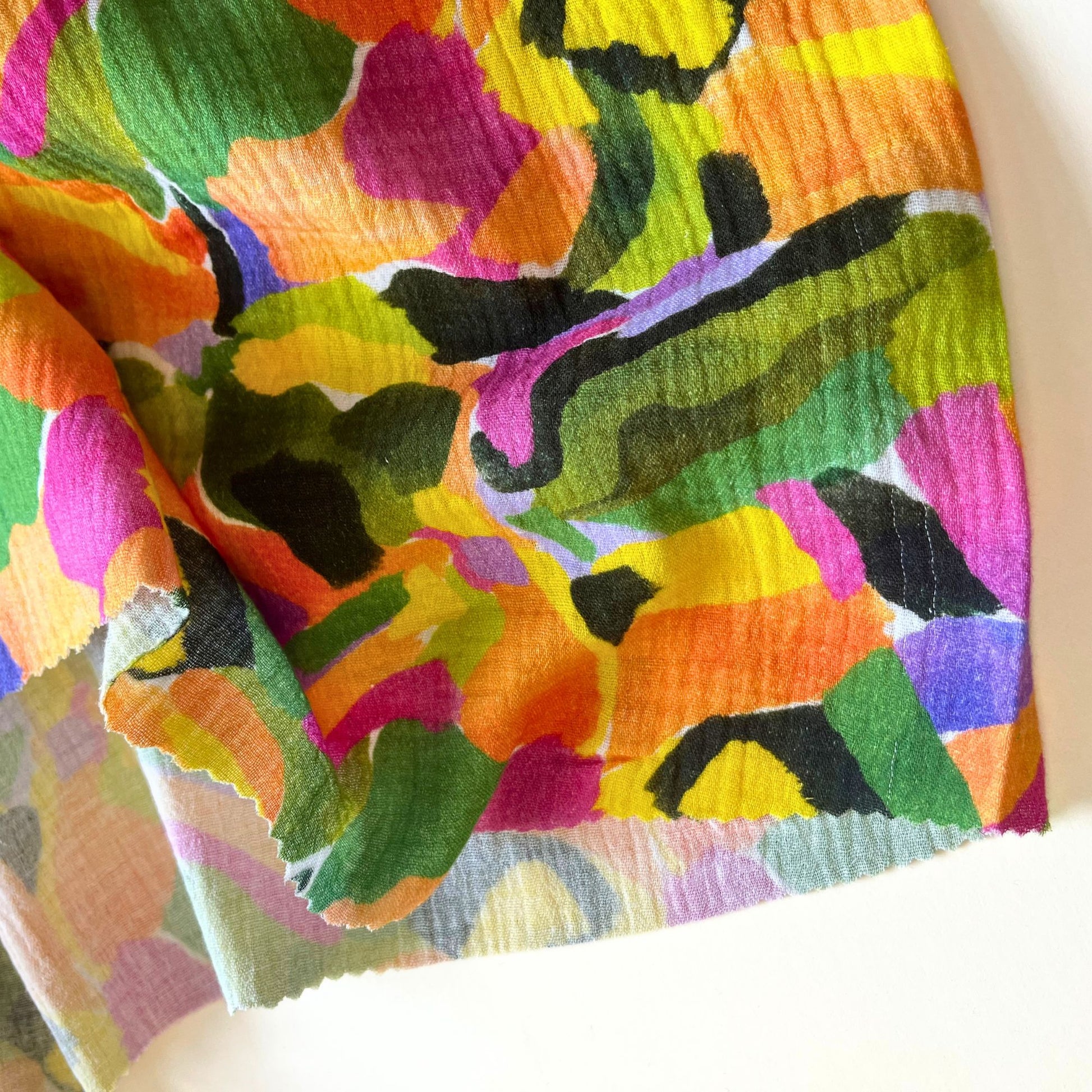 Tropical Palette double gauze in white with painterly green, purple and orange botanical streaks folded to show soft two-layer cotton construction — lightweight airy fabric ideal for handmade dresses, blouses, baby muslins and children's playsuits