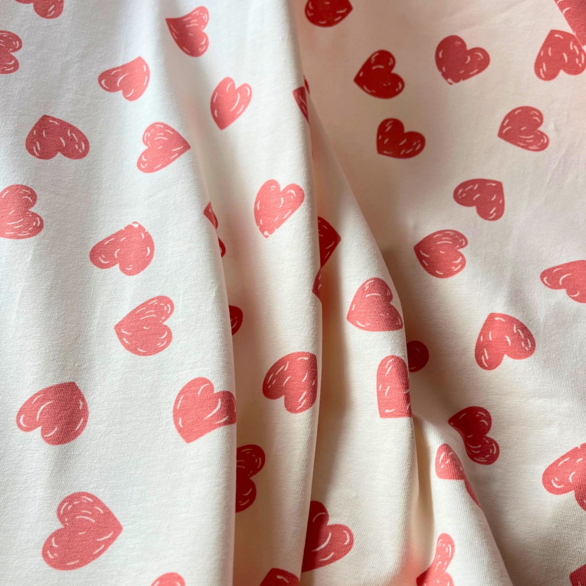 Doodle hearts print stretch jersey in cream with rose pink hand-drawn hearts folded to show soft knit construction — breathable cotton elastane fabric ideal for handmade children's clothing, loungewear and baby gifts