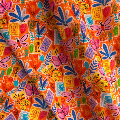 Orange Postcard Garden cotton fabric folded to show crisp woven construction and layered scattered print of postcards, botanicals and butterflies — breathable 100% cotton ideal for handmade blouses, skirts and summer dresses