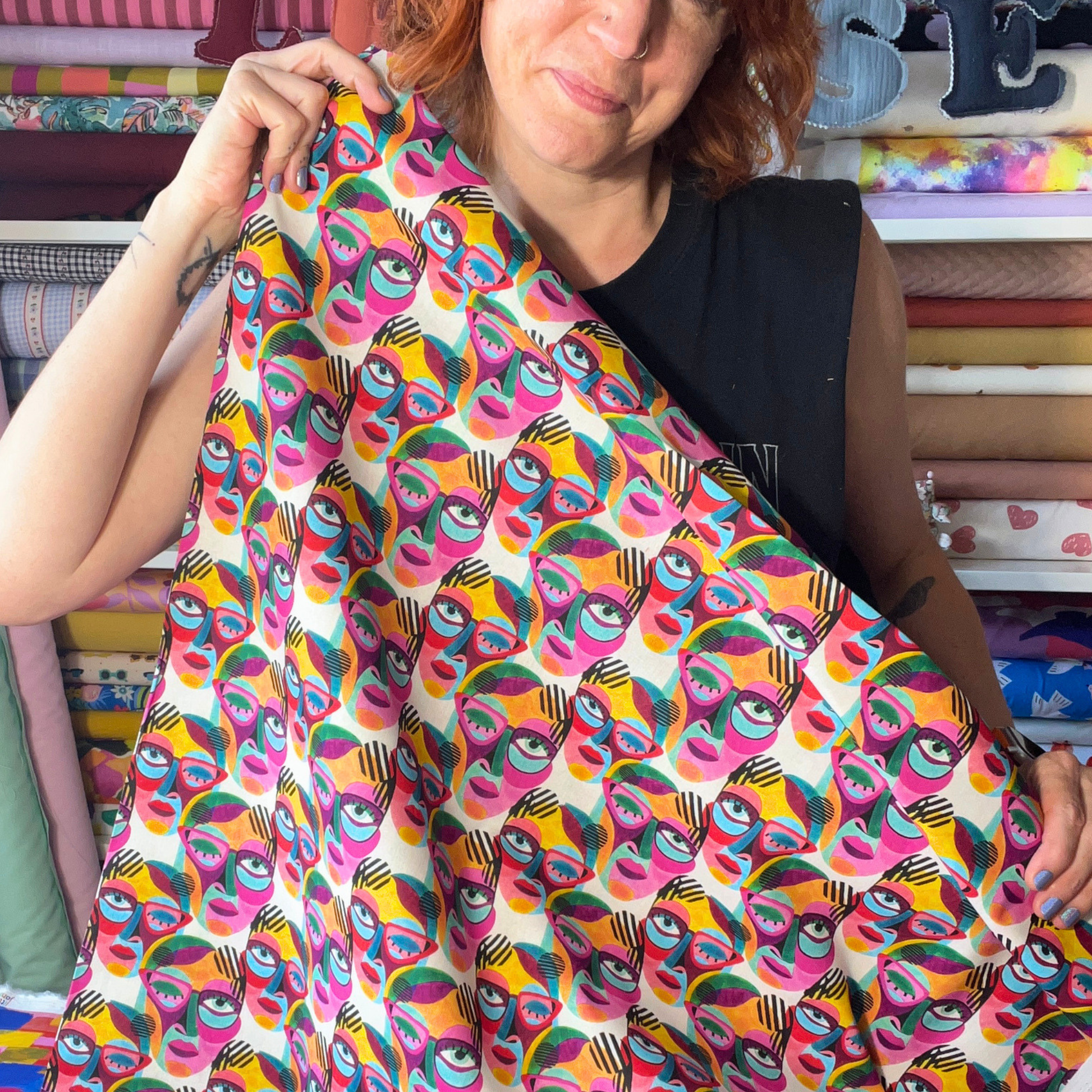 Little Johnny abstract faces cotton fabric held up to show crisp drape and scale of painted face print on white base — statement dressmaking fabric ideal for handmade wrap dresses, midi skirts and conversation piece co-ords