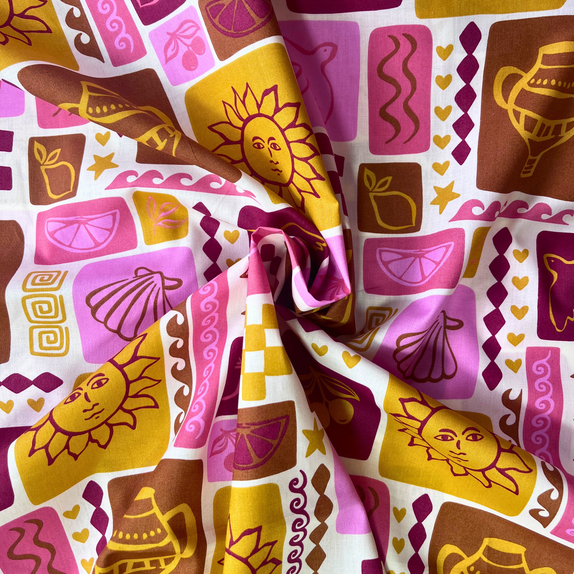 Summer patchwork print cotton poplin from Poppy Fabrics folded to show crisp woven construction and warm holiday inspired print of shells, suns, birds and fruit in pink, red, mustard and ginger tones — lightweight breathable fabric ideal for handmade blouses, midi skirts and summer dresses