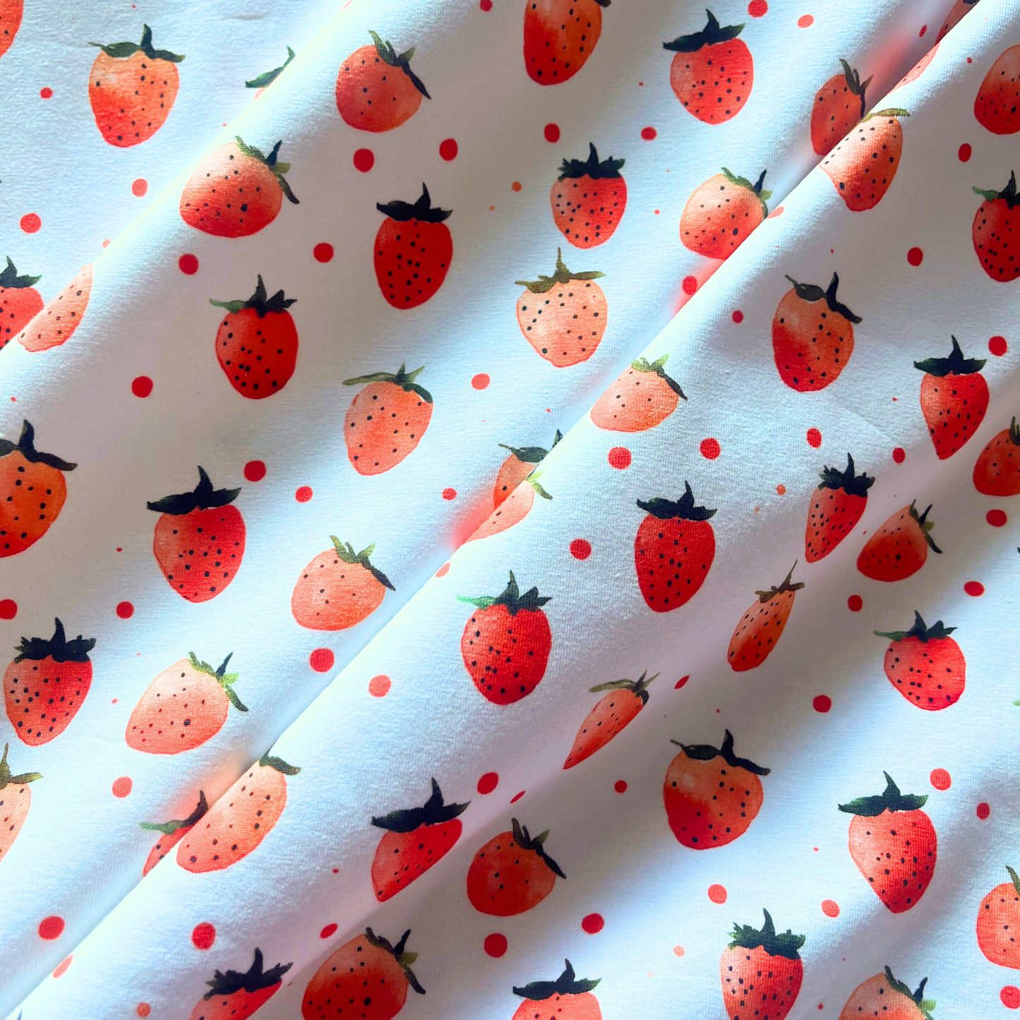 Close-up of cream stretch jersey fabric showing digitally printed red strawberry design — Oeko-Tex certified 200gsm cotton elastane knit, soft and breathable for babywear and children's sewing