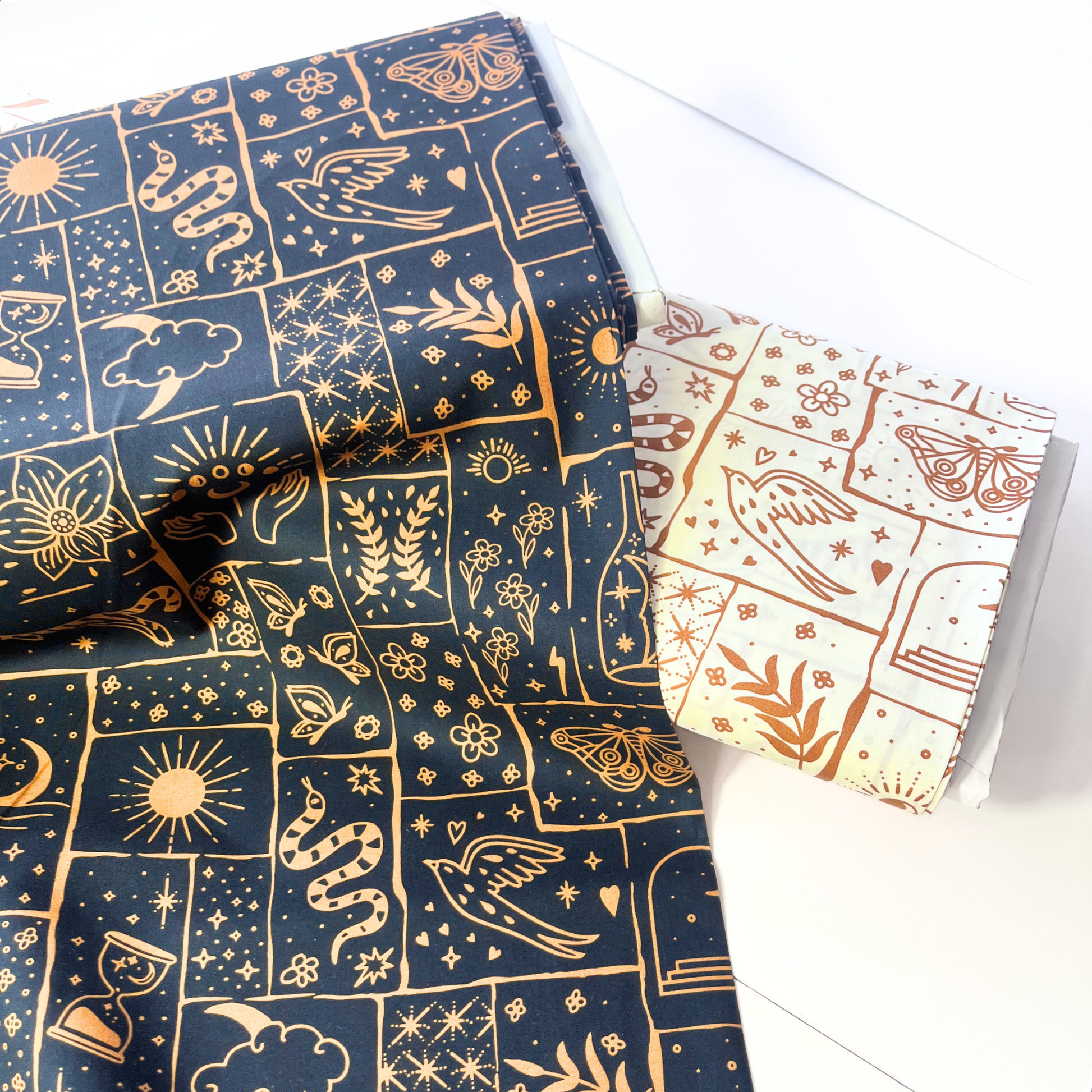 Flat lay of black base celestial patchwork poplin fabric draped to show crisp lightweight 110gsm drape — irregular caramel and ginger patches with tigers, florals and moons, perfect for handmade shirt dresses and statement co-ords

