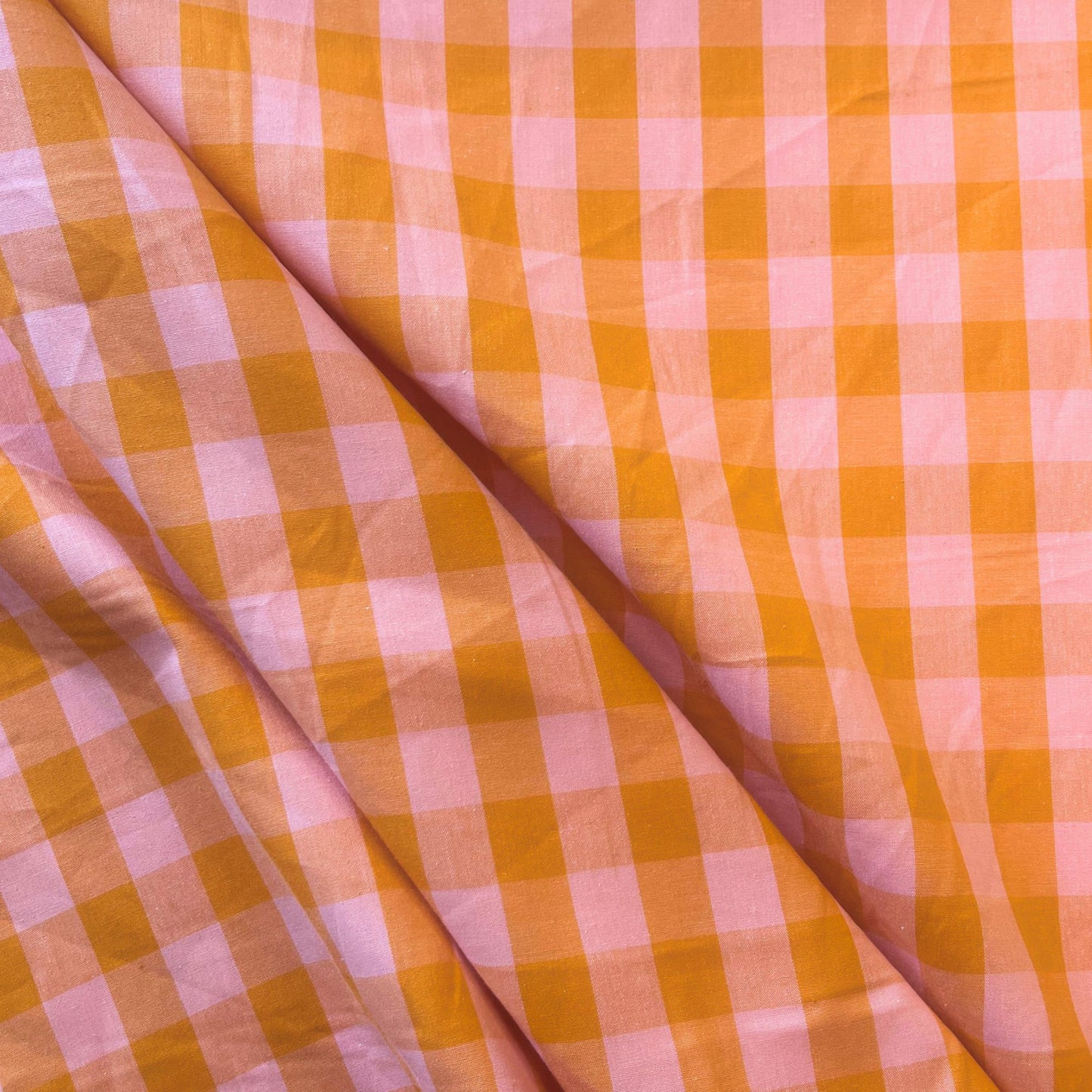 Flat lay of orange and salmon gingham check fabric draped to show lightweight 115gsm drape and generous 145cm width — yarn dyed cotton woven perfect for summer dresses and children's clothing