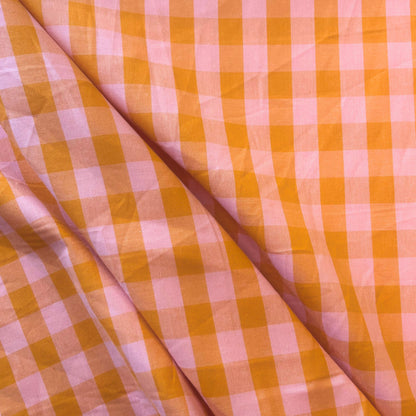 Flat lay of orange and salmon gingham check fabric draped to show lightweight 115gsm drape and generous 145cm width — yarn dyed cotton woven perfect for summer dresses and children's clothing