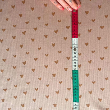 Fabric with heart pattern and a measuring tape showing measurements.