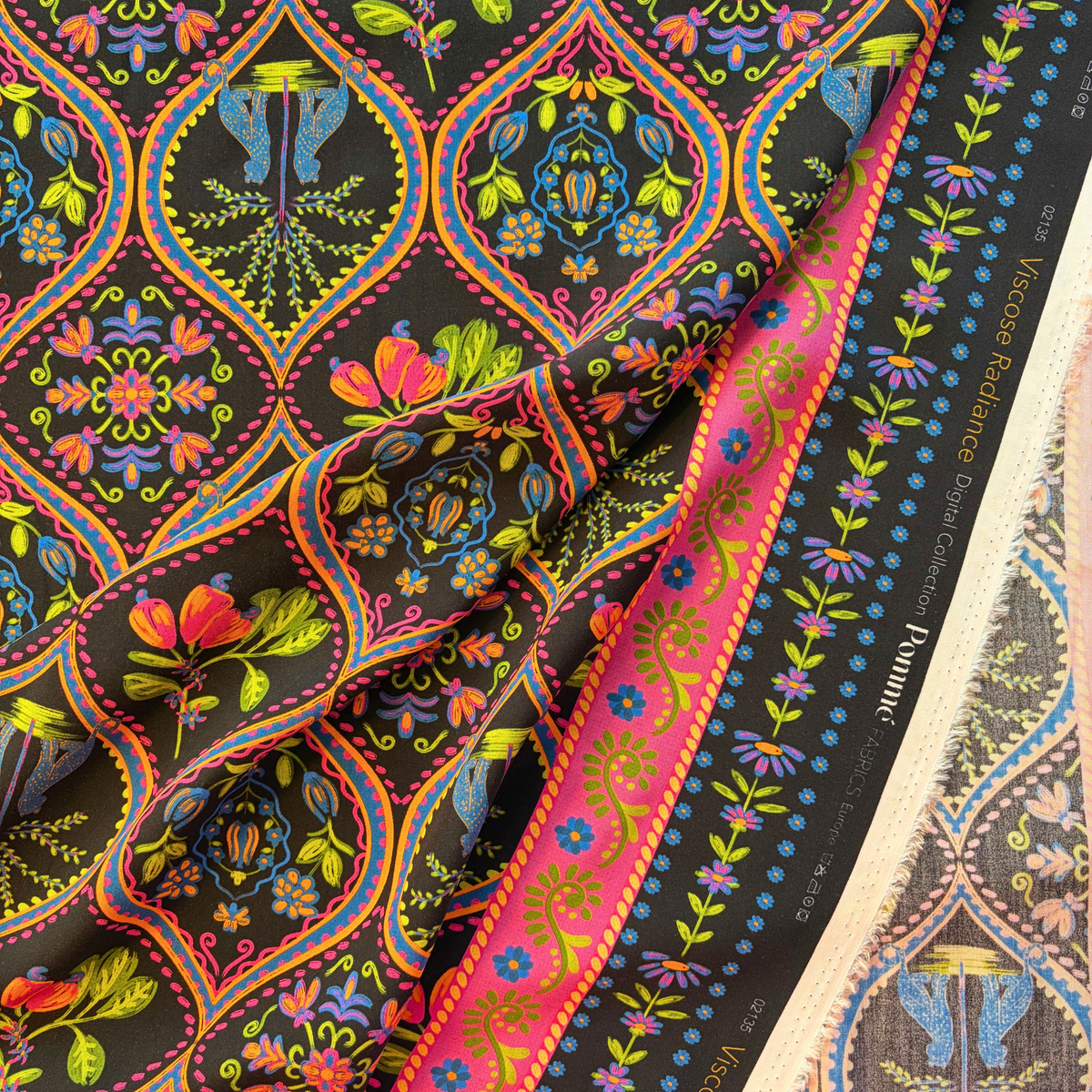Black bohemian tropical digital viscose woven fabric folded to show fluid drape and vivid leopard palm print in pink purple blue green and orange — 142cm wide lightweight dressmaking fabric for wrap dresses skirts and kimono jackets