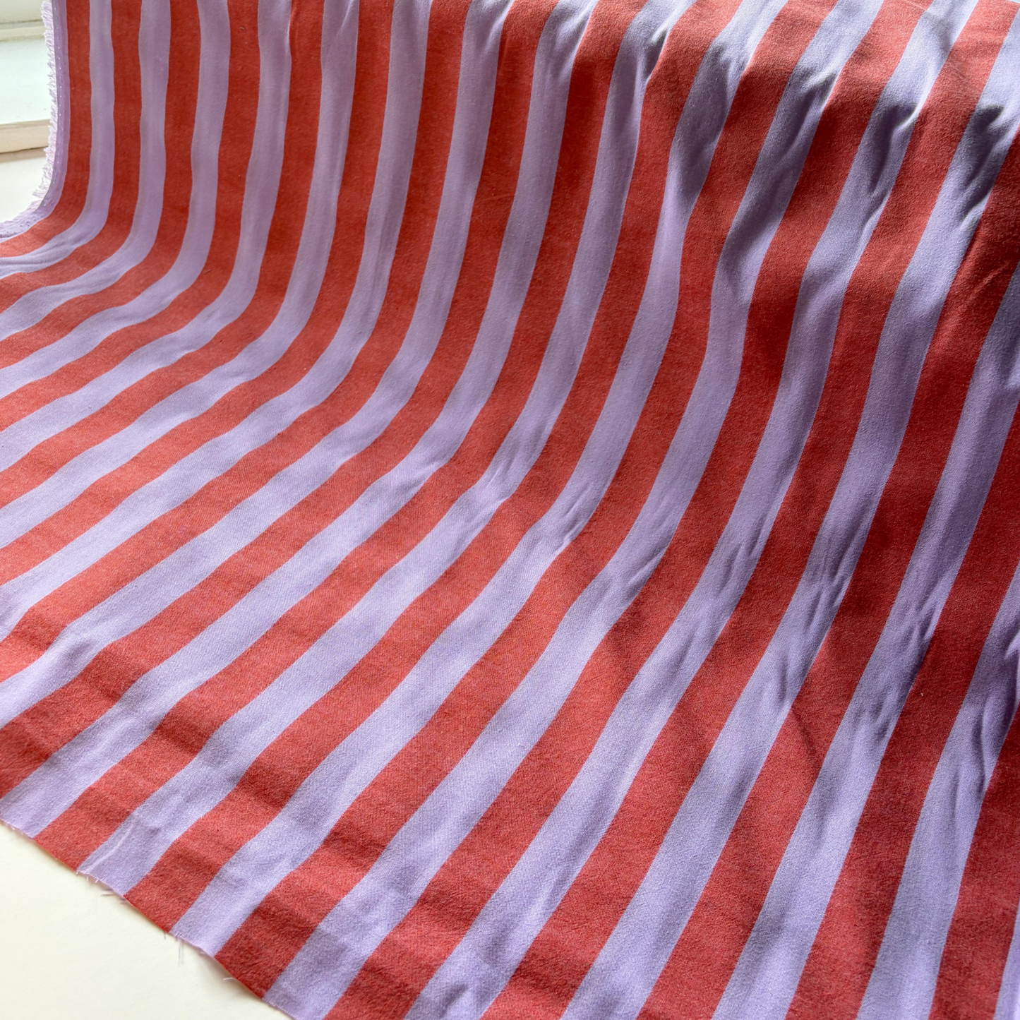 Burnt orange and lavender vertical stripe yarn dyed cotton fabric folded to show woven construction — 2.2cm stripe 145cm wide Oeko-Tex certified lightweight dressmaking fabric for blouses pinafores and summer dresses