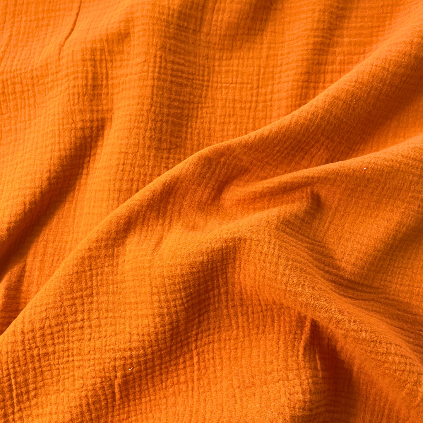 Close-up of burnt orange plain double gauze fabric showing soft two-layer organic cotton construction — GOTS certified 125gsm woven ideal for handmade children's dresses, baby swaddles and adult blouses