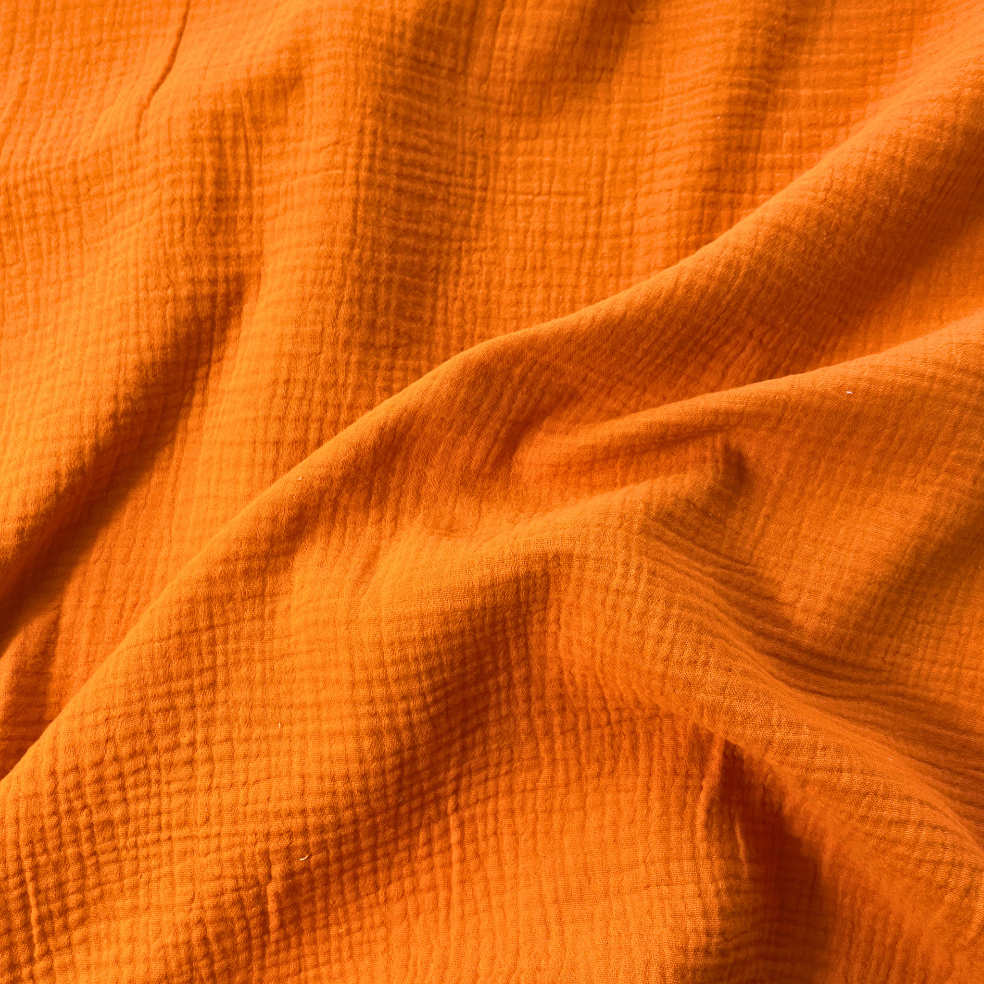 Close-up of burnt orange plain double gauze fabric showing soft two-layer organic cotton construction — GOTS certified 125gsm woven ideal for handmade children's dresses, baby swaddles and adult blouses