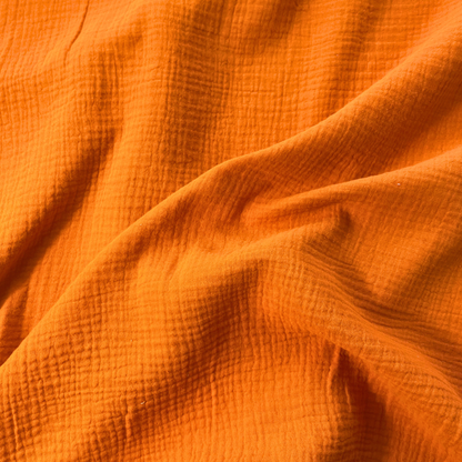 Close-up of burnt orange plain double gauze fabric showing soft two-layer organic cotton construction — GOTS certified 125gsm woven ideal for handmade children's dresses, baby swaddles and adult blouses